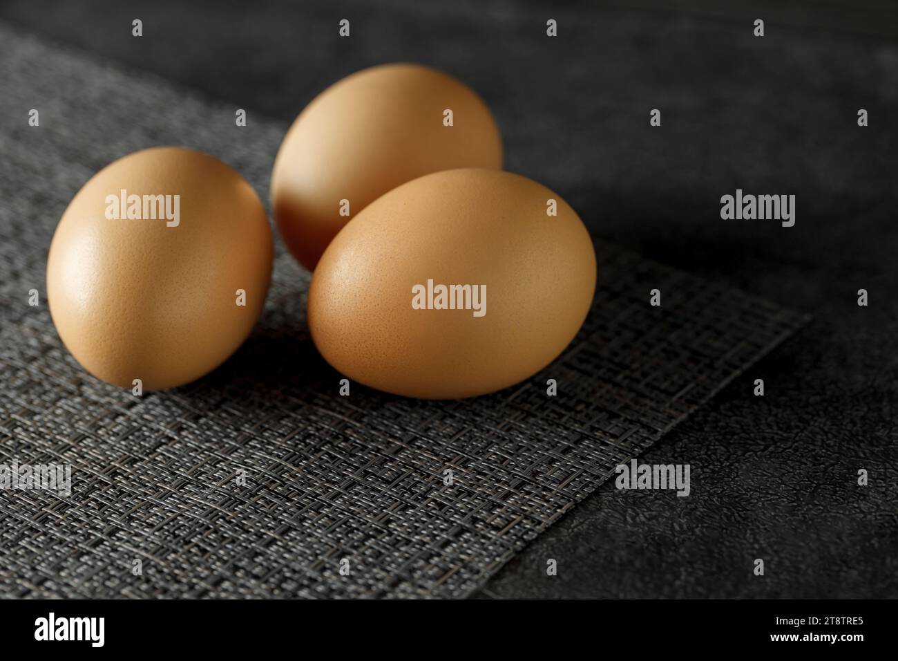 Three whole chicken eggs on dark surface, selective focus. Stock Photo