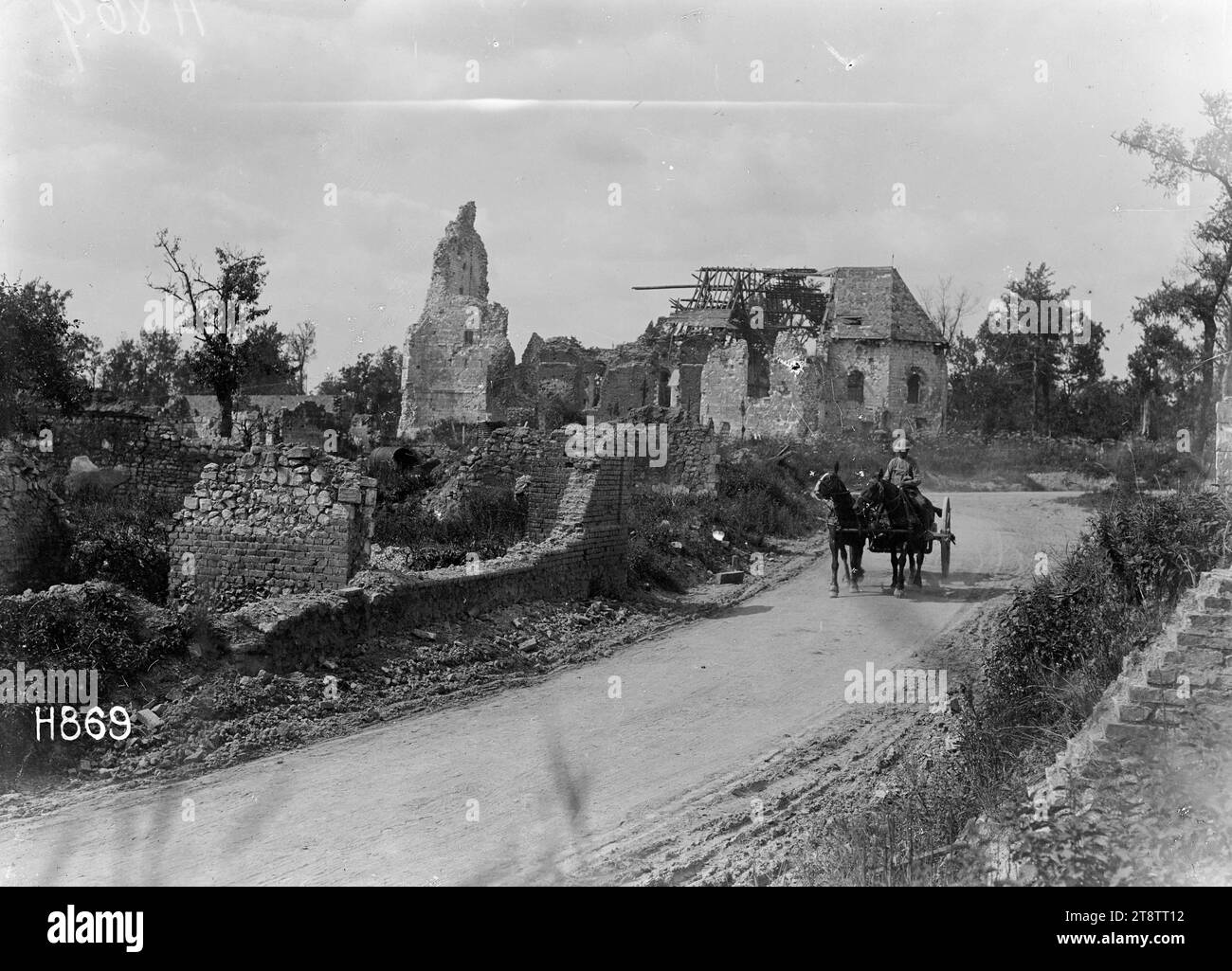 A badly shelled, scarred French village just behind the lines, World War I, A badly shelled and scarred French village (unidentified) just behind the lines in World War I. View looking over a road at the ruins of brick buildings and houses. A soldier drives a cart down the road. Photograph taken 11 August 1918 Stock Photo