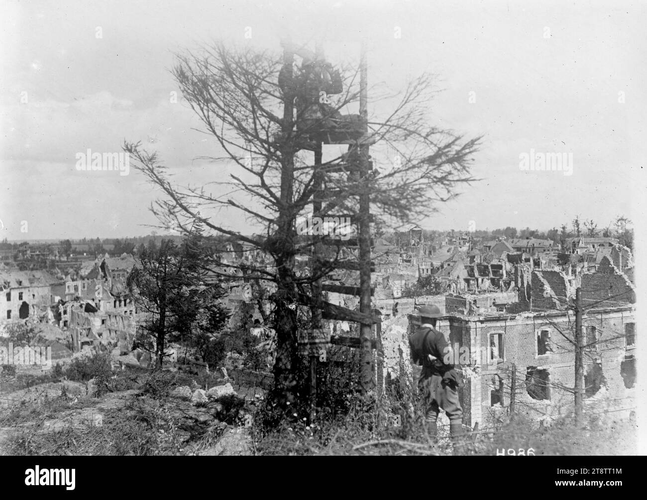 A German Artillery observation post in Bapaume, World War I, A wooden German artillery observation post among trees on high ground overlooking Bapaume, after the town's capture in the Battle of Bapaume. A New Zealand soldier looks at the wide view from the top of the post and another soldier looks over the ruined town from the foot of it. Photograph taken 29 August 1918 Stock Photo
