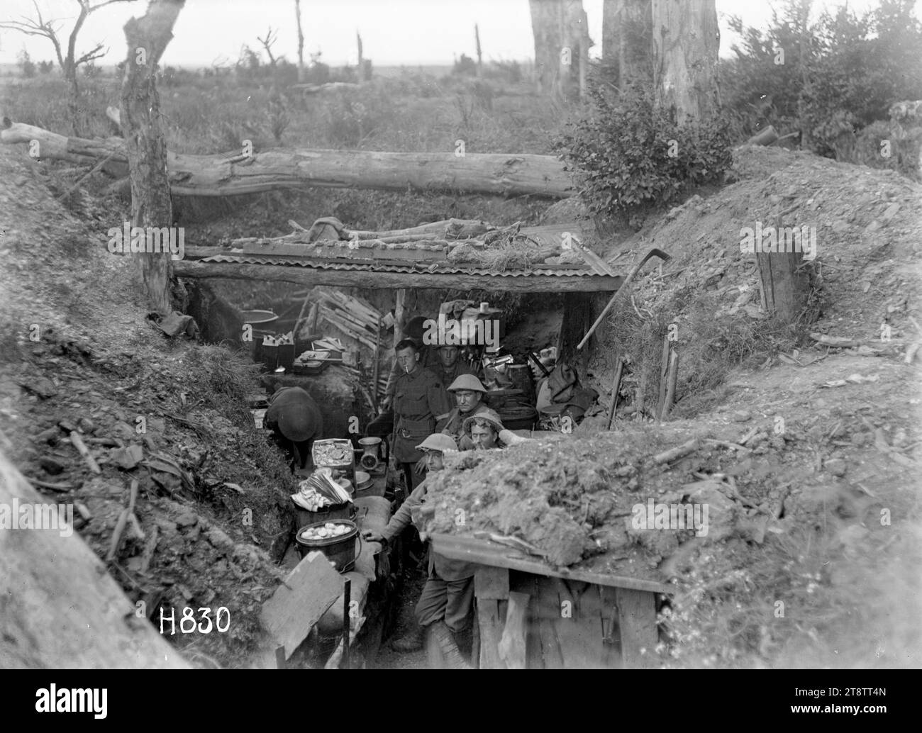 Preparing a meal in the trenches near Gommecourt, World War I, A view looking down into a trench which temporarily houses the company cookhouse of the New Zealand Rifle Brigade, near the front during World War I. Helmeted soldiers prepare meals in very cramped conditions with only pieces of wood and corrugated iron above for protection. A large iron pot full of potatoes? and a meat grinder are visible in the foreground. Photograph taken near Gommecourt, France, 25 July 1918 Stock Photo