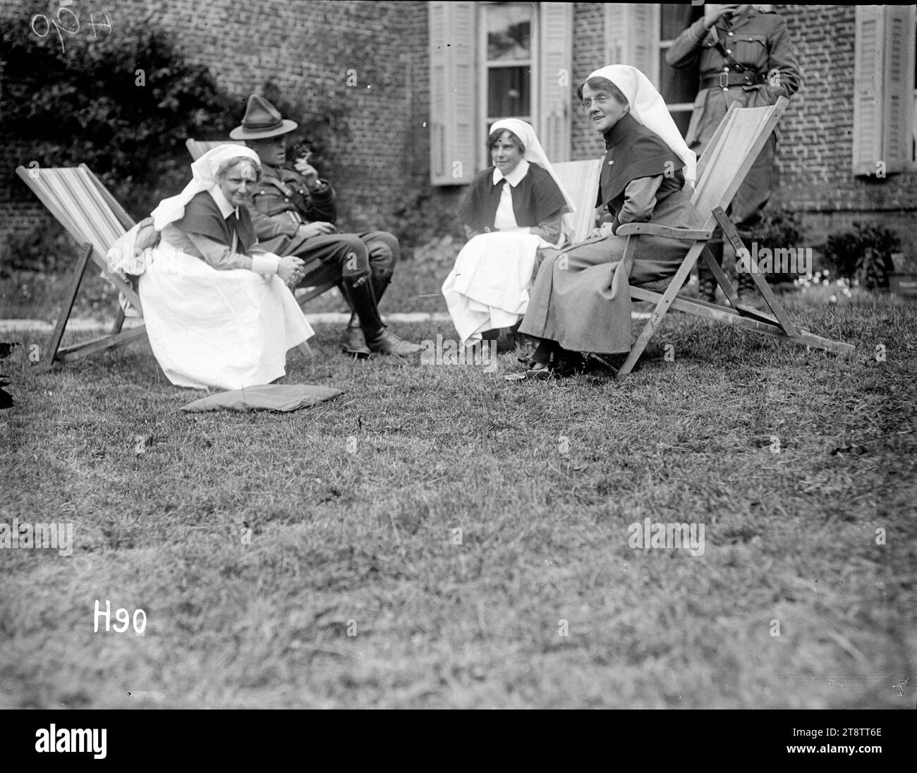 Matron Price at a garden party in the grounds of the New Zealand Stationary Hospital, France, Matron Frances Price, sitting in a deck-chair at right, talks with nurses and a soldier at a garden party in the grounds of the New Zealand Stationary Hospital, probably at Hazebrouck, during World War I. The nurses have been identified as Miss Scott and Sister Whittes. Photograph taken 24 June 1917 Stock Photo