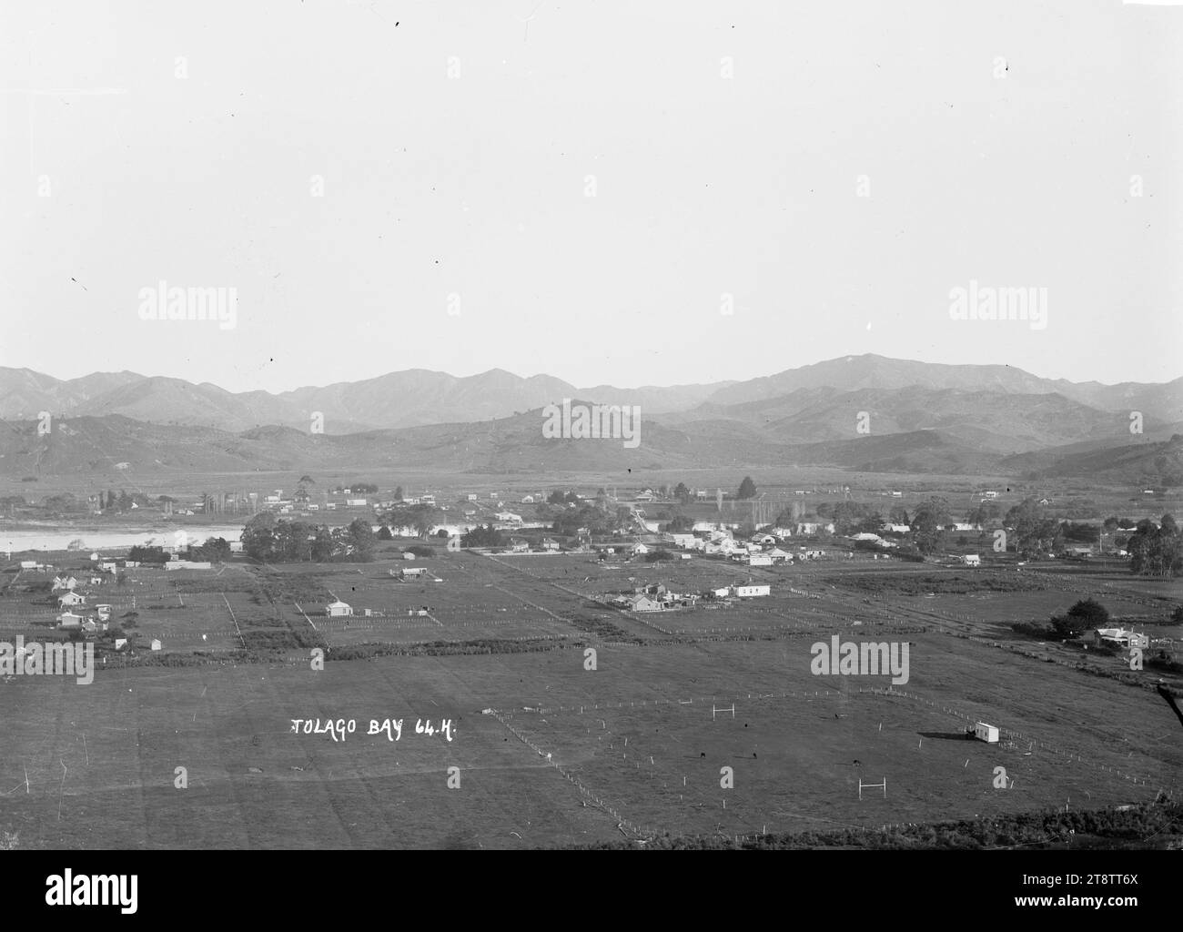 Distant view of Tolaga Bay, Gisborne, Distant view of Tolaga Bay, Gisborne. Shows the town beside the river, with farm houses and paddocks in the foreground (including one used as a rugby field). A mountain range can be seen in the distance. Photograph taken between 1906 and 1912 Stock Photo