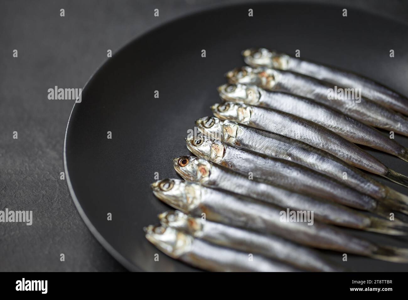Anchovy european, hamsa fresh, source of omega 3, several small fish laid on gray plate, on dark background, selective focus. Stock Photo