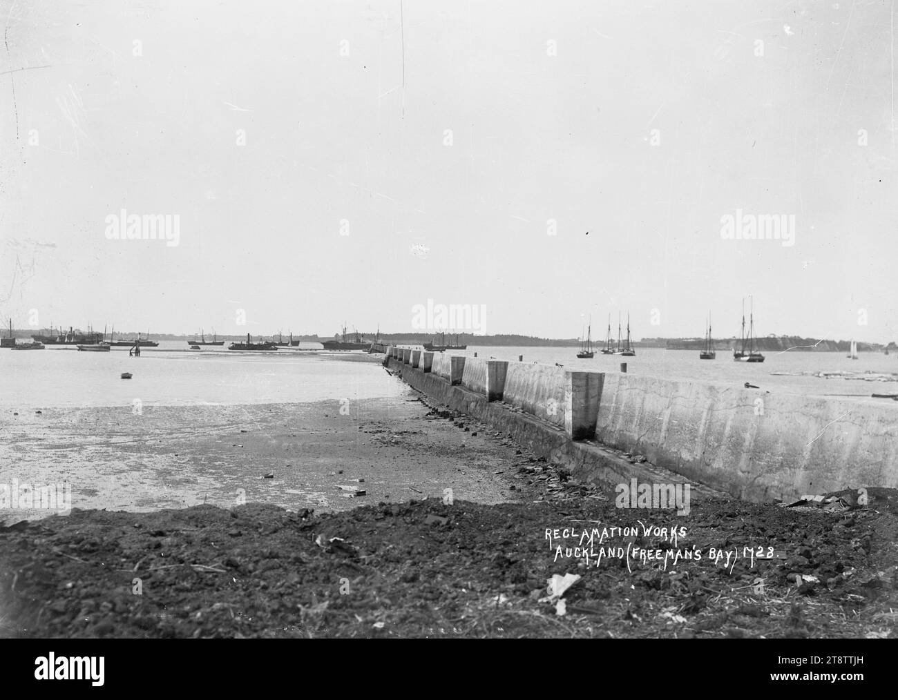 Reclamation works at Freemans Bay, Auckland, New Zealand, View of Freemans Bay taken from the shore looking out over the tidal flats to the Waitemata Harbour in the distance where ships and a dredge are anchored. On the right is a concrete wall which extends out into the bay. in the early 1900s before the reclamation work for wharf development had been completed Stock Photo