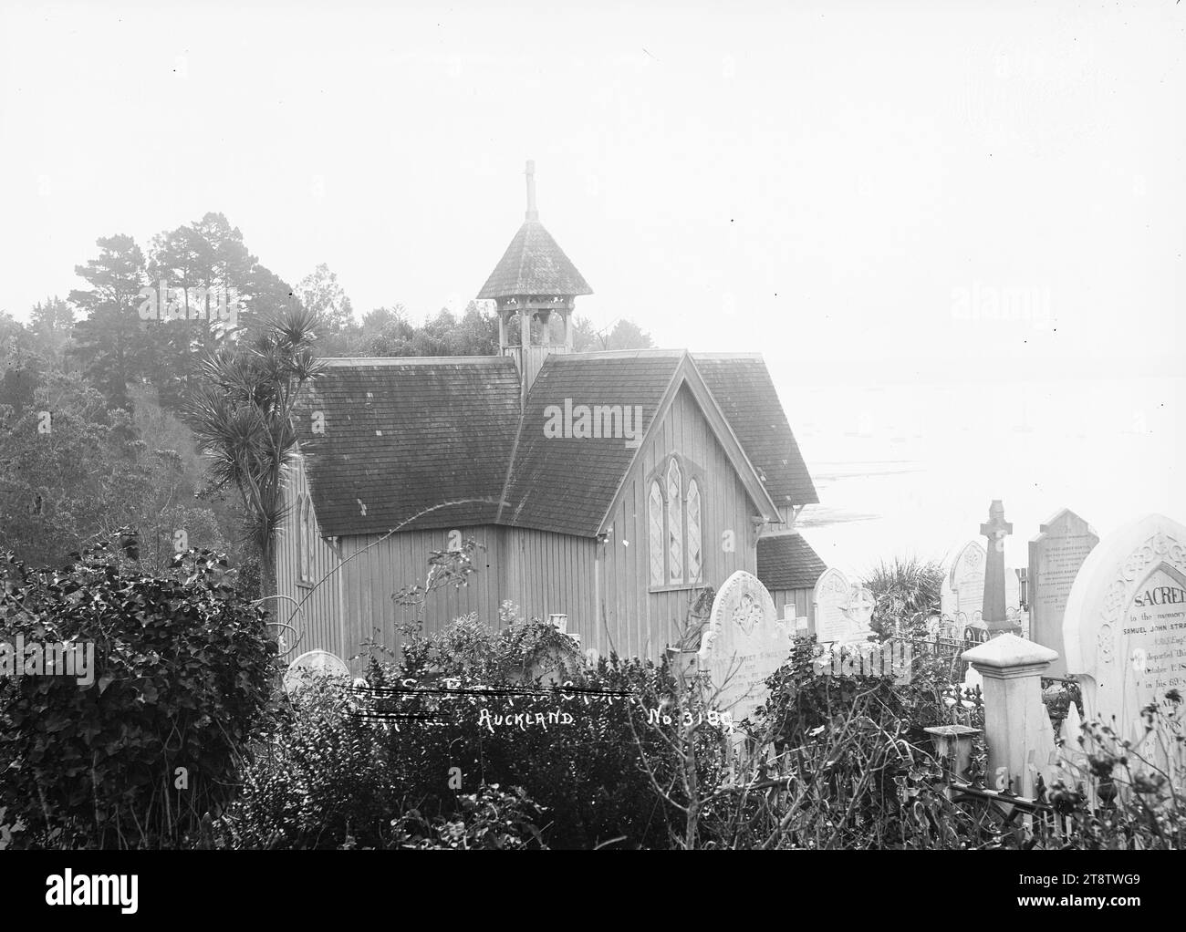 St Stephen's Church and burial ground, Judges Bay, Parnell, View of St Stephen's Church looking north west over Judges Bay towards the city in the distance. In the foreground is the graveyard. Headstones belonging to Vicesimus Lush (d 1882), Samuel John Stratford (d 1871), and members of the Sinclair and Morton families are identifiable from the inscriptions. ca 1910 Stock Photo