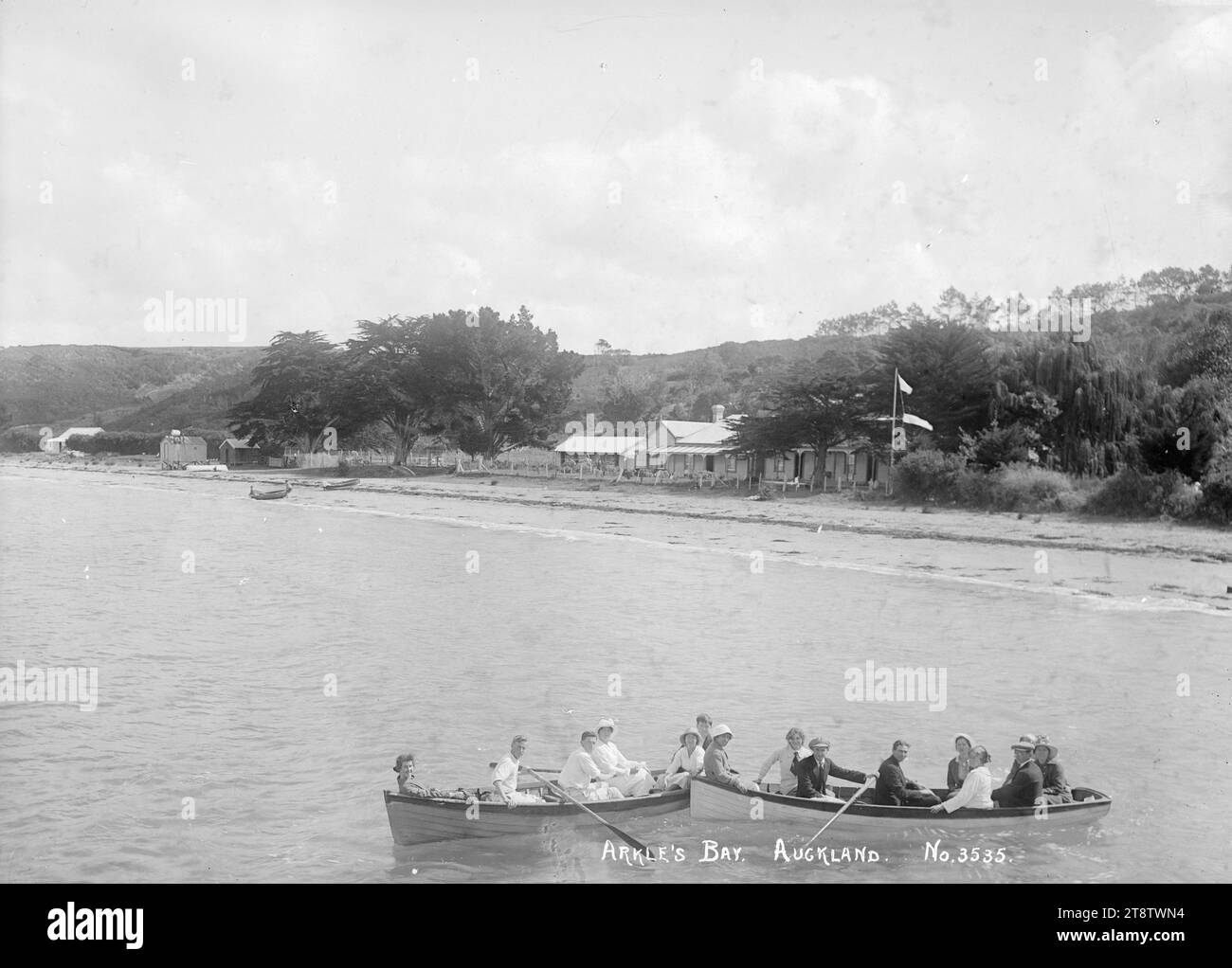 Row boats at Arkles Bay, Auckland, New Zealand, Two boat loads of people rowing in Arkles Bay in front of Arkle's Bay House. A flagpole can be seen on the right of Arkle's Bay House. Taken in early 1900s (possibly from the jetty at the north end of the bay Stock Photo