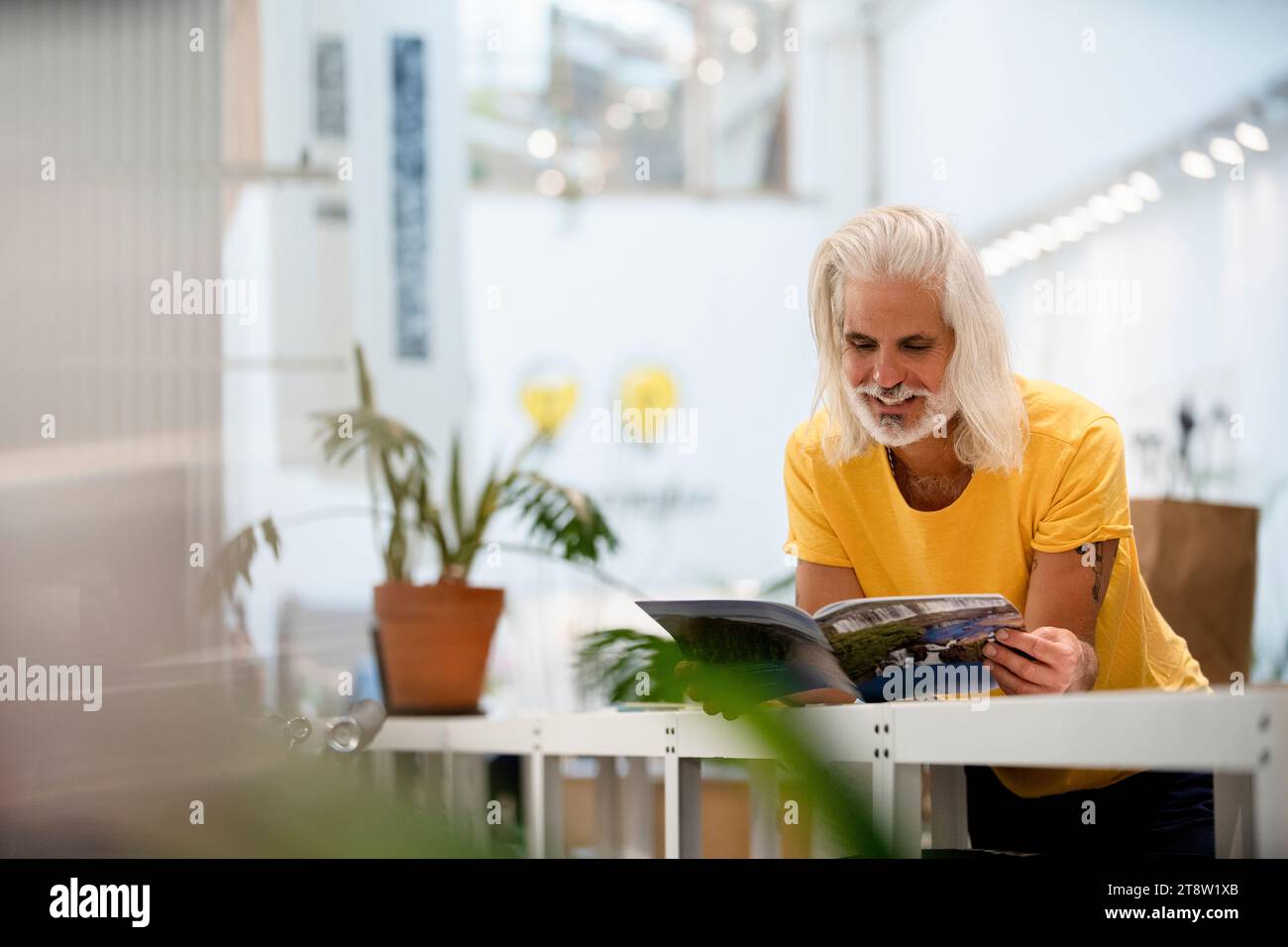 Adult male designer leaning on table while reading magazine Stock Photo