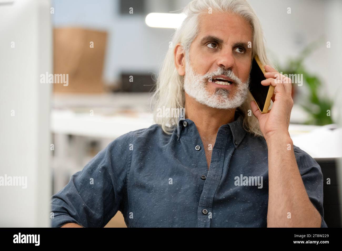 Free lance designer talking on smart phone while working on computer Stock Photo
