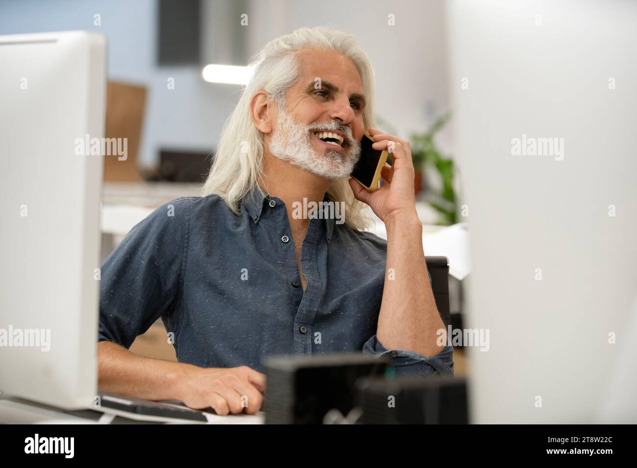 Free lance designer talking on smart phone while working on computer Stock Photo