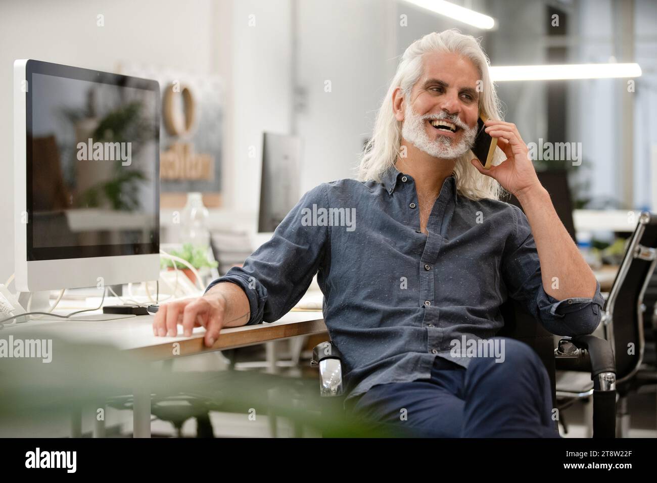 Free lance designer talking on smart phone while working on computer Stock Photo