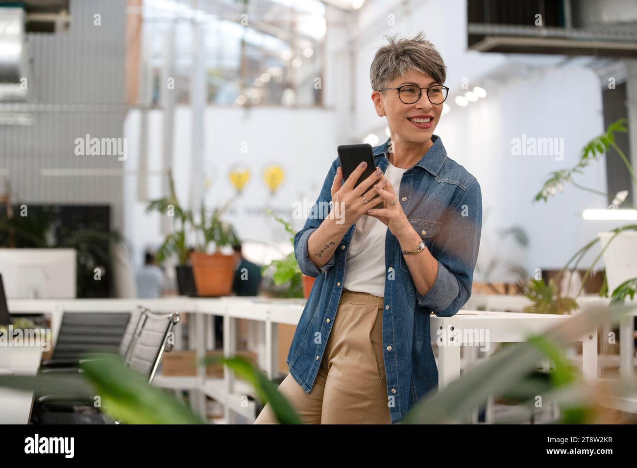 Female entrepreneur using smart phone while standing indoors Stock Photo