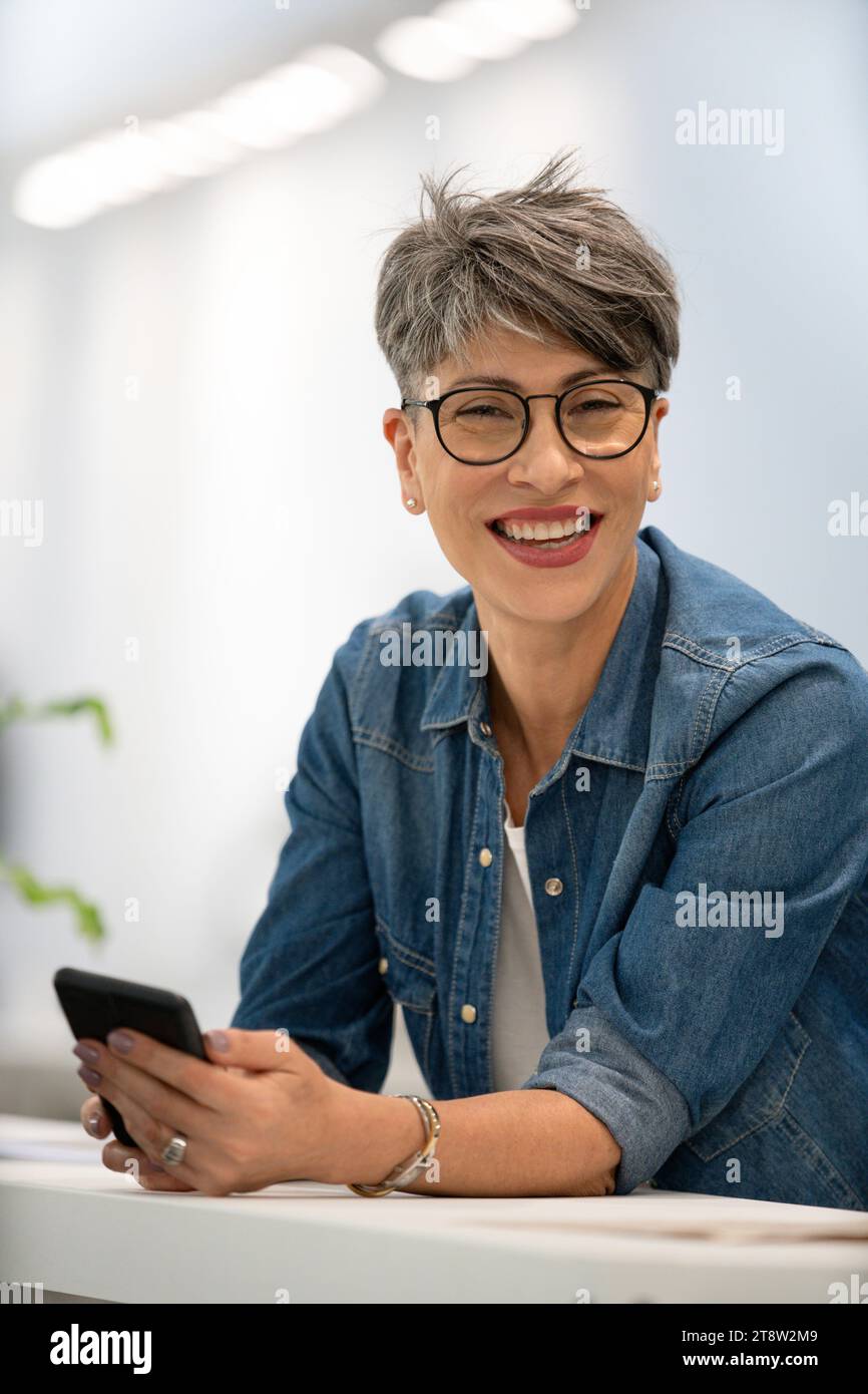 Female designer using smart phone while looking at the camera Stock Photo