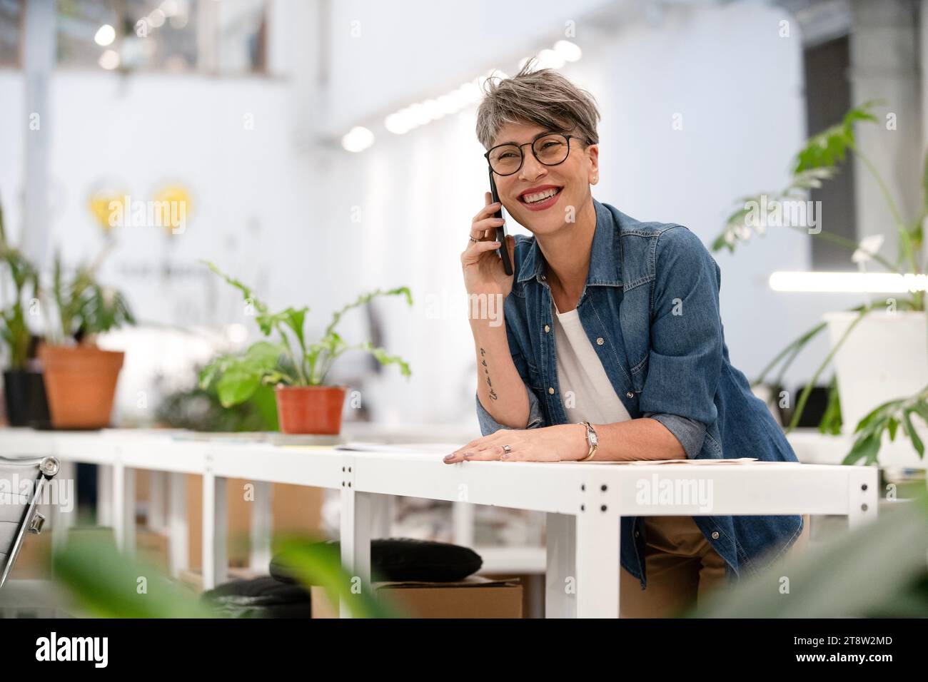 Female designer listening to voice mail while leaning on table Stock Photo
