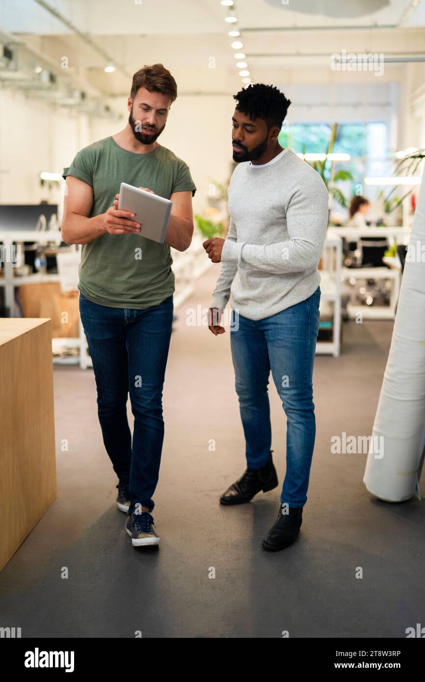Two coworkers standing while discussing over digital tablet Stock Photo
