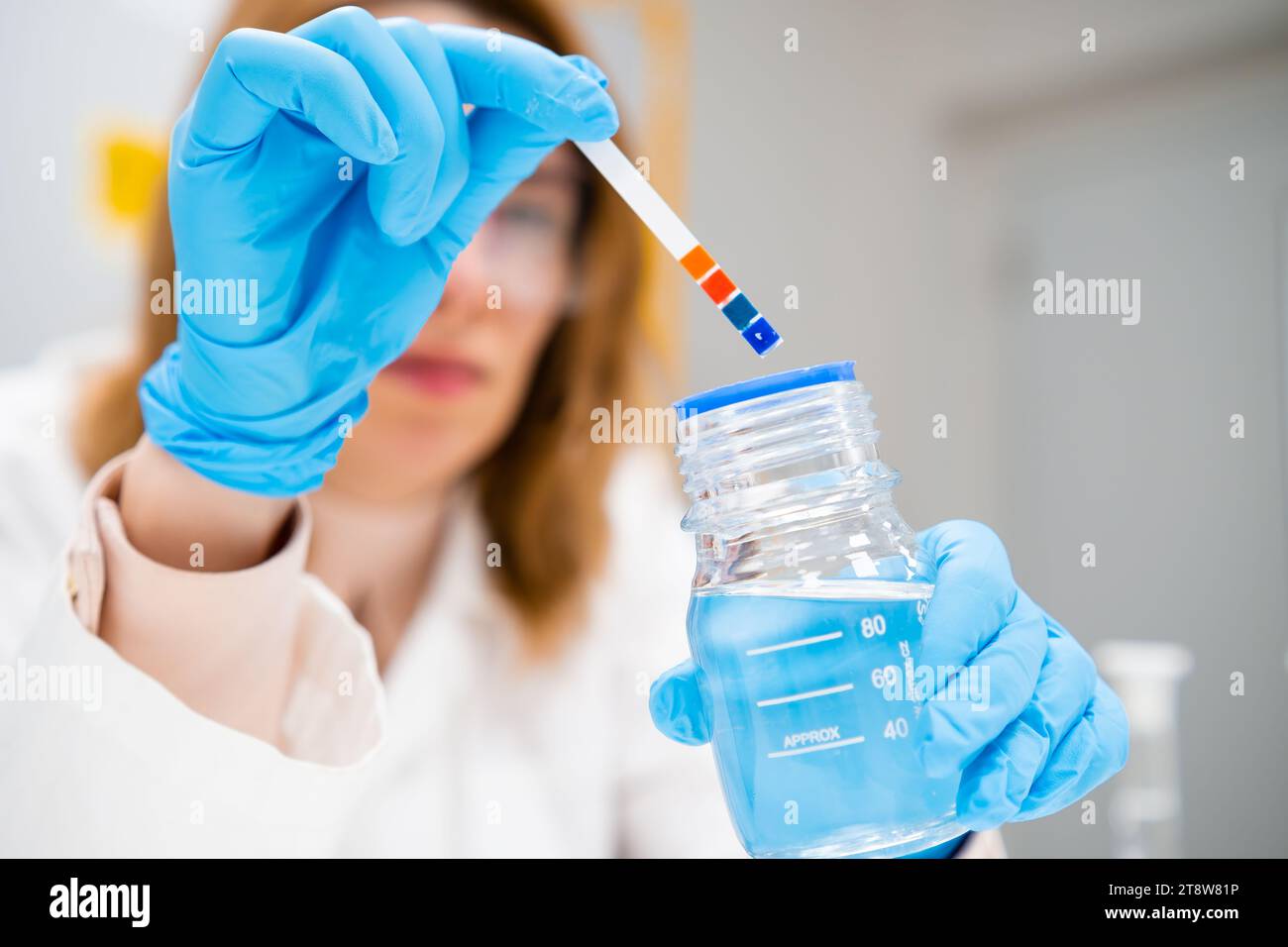 Female scientist measures pH of the solution using indicator paper Stock Photo