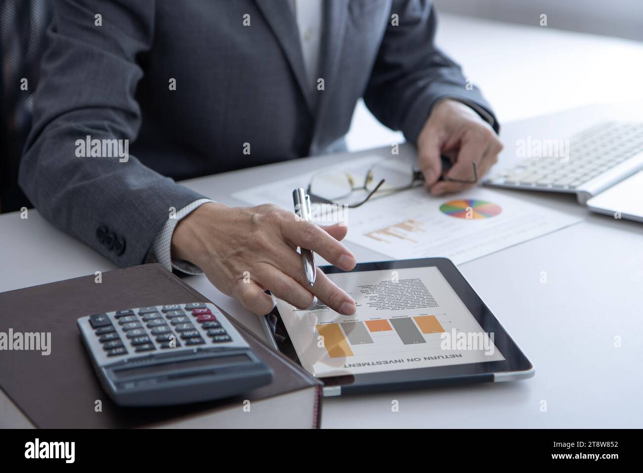 Businessman in the office tabbing on tablet screen while reveiwing business performance for return on investment Stock Photo