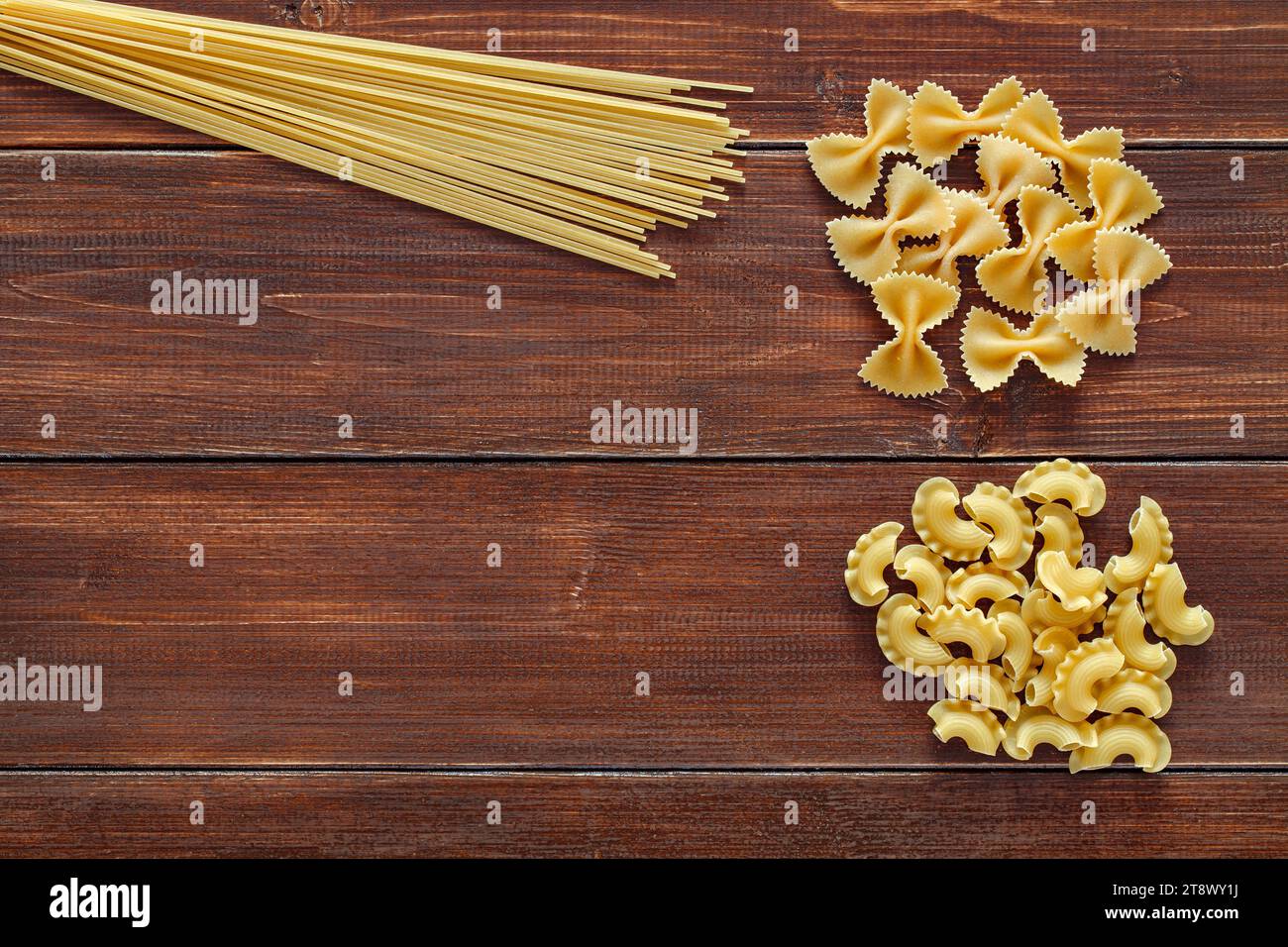Spaghetti, maccheroni raw, farfalle, cresta di gallo, on wooden brown planks dark background, top view, space to copy text. Stock Photo