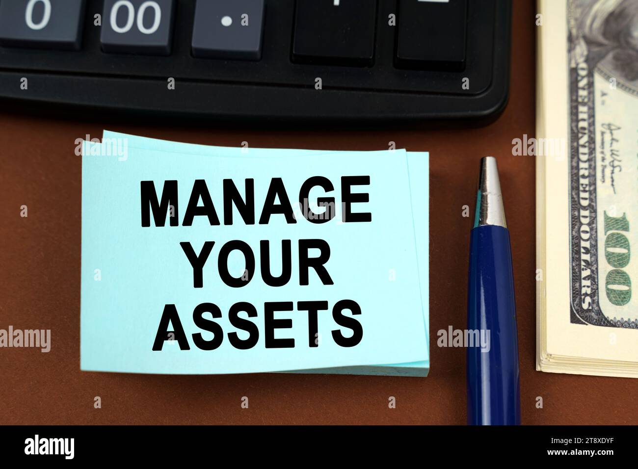 Business concept. On a brown surface lies a calculator, dollars, pens and stickers with the inscription - manage your assets Stock Photo