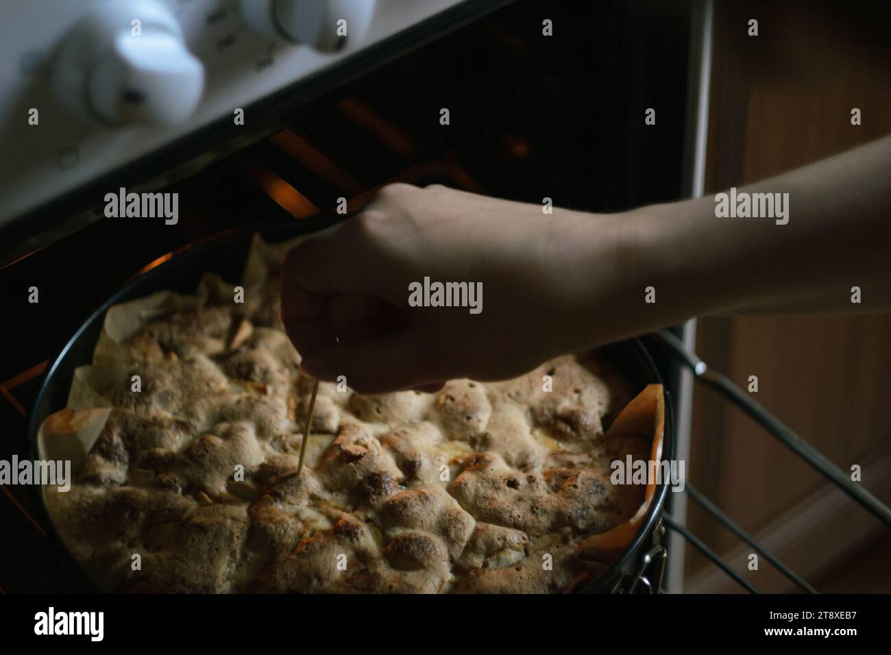 Female hands check the readiness of Charlotte apple pie and open the oven Stock Photo
