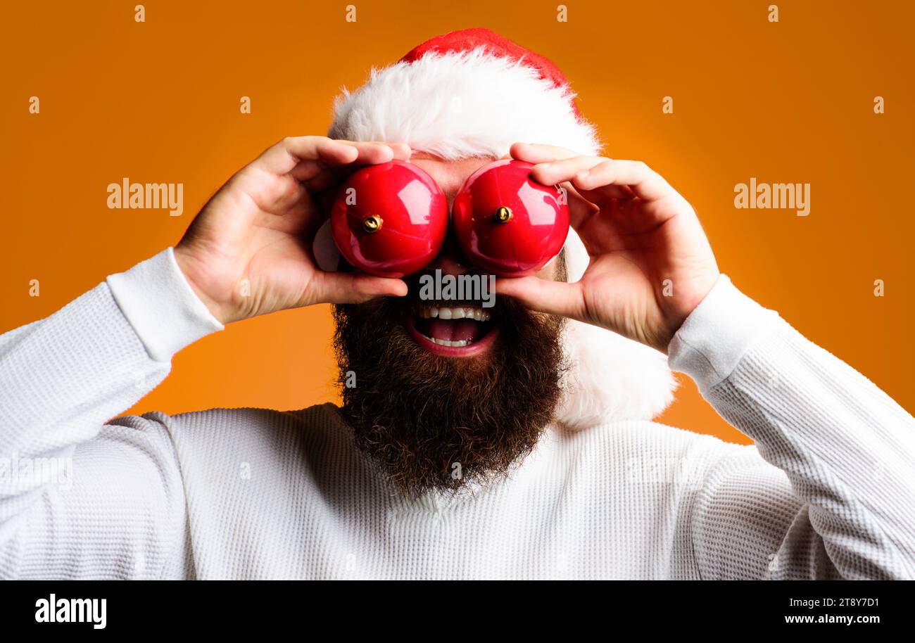 Merry Christmas and Happy New Year. Santa man with red Christmas balls near eyes. Festive decoration for Christmas tree. Happy bearded man in Santa Stock Photo