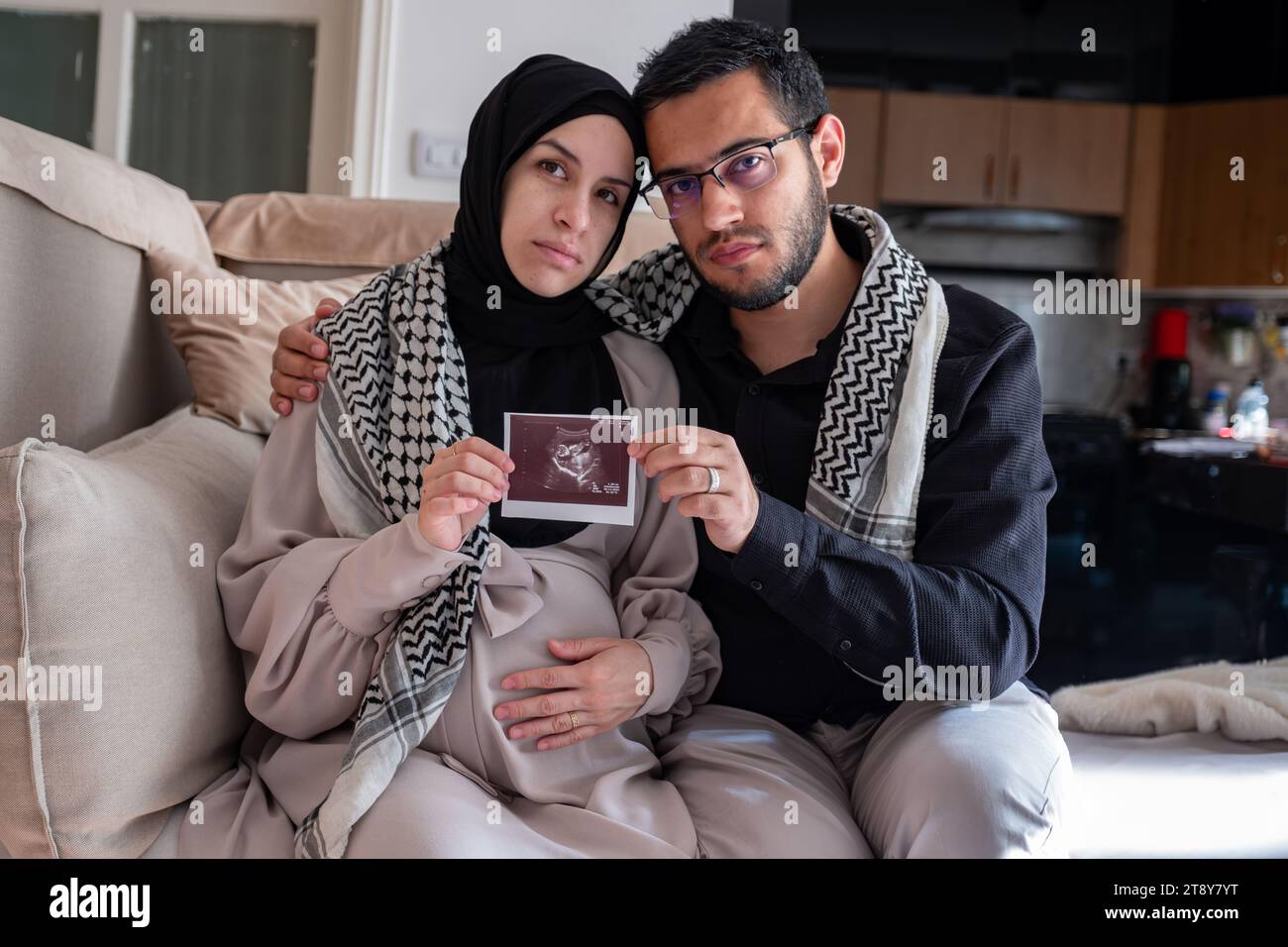 Husband and his wife holding sonography photo for there fetus while wearing palestinian keffiyeh in living room Stock Photo