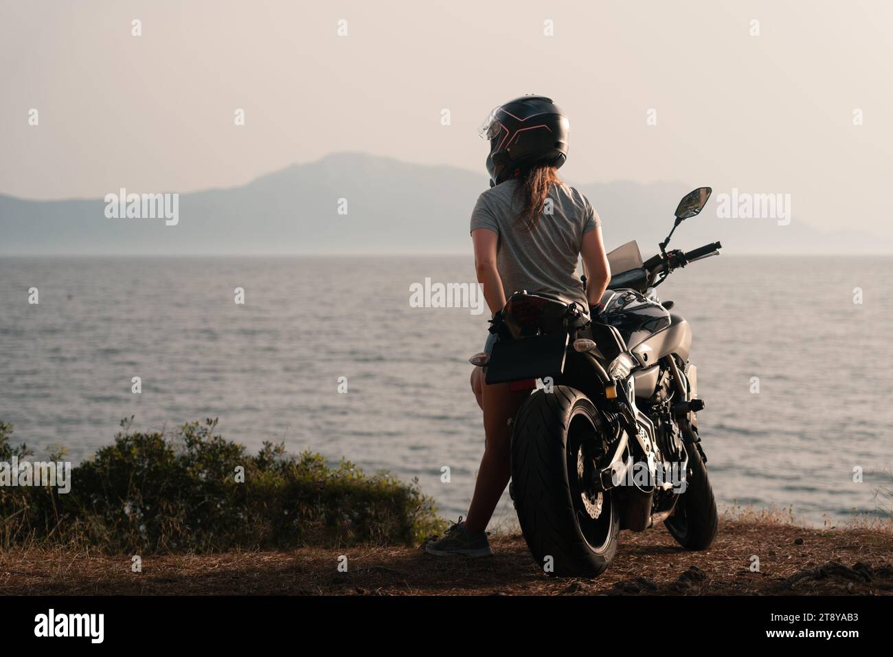 woman leaning on a motorcycle an looking at the sea Stock Photo
