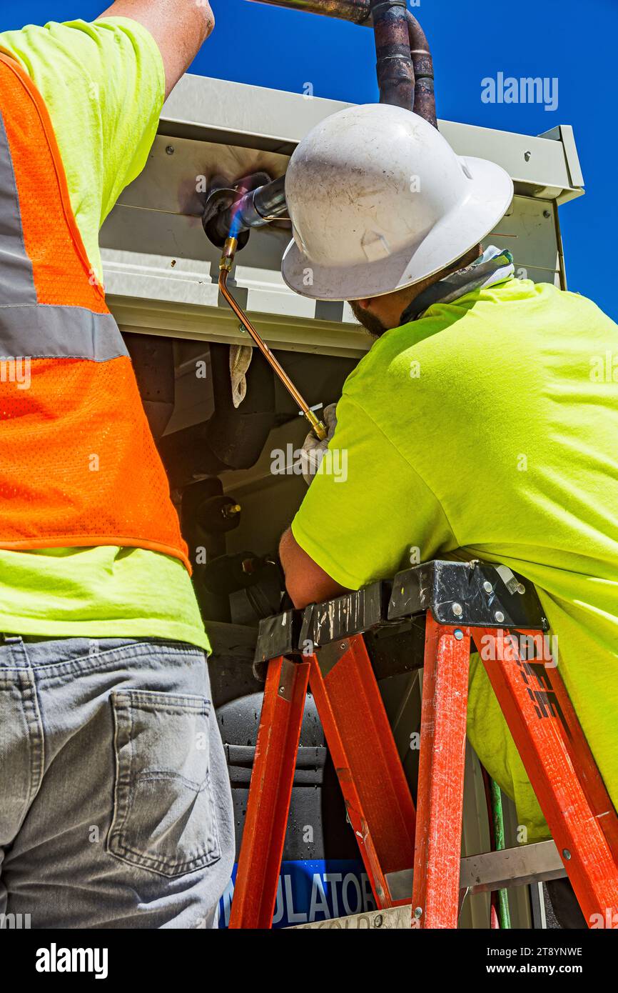 Construction workers brazing copper pipes at a compressor housing on
