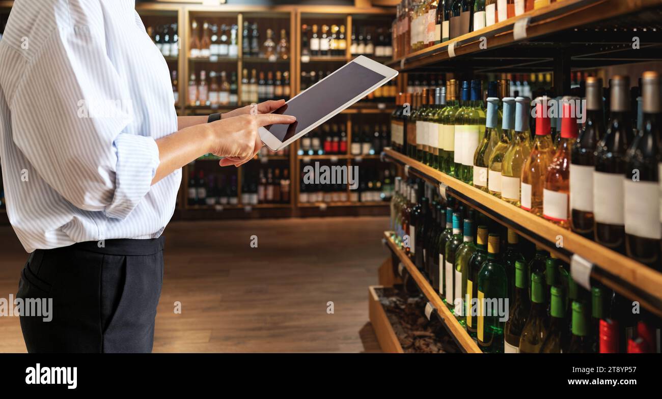 Liquor store manager inventories product using digital tablet. Stock Photo