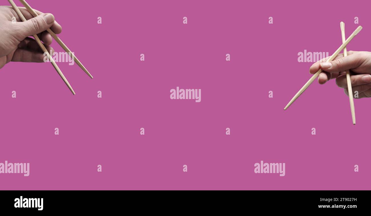 Asian chopsticks held in human hands on monochrome dark pink background. Without food. No identifiable person. Copy space Stock Photo