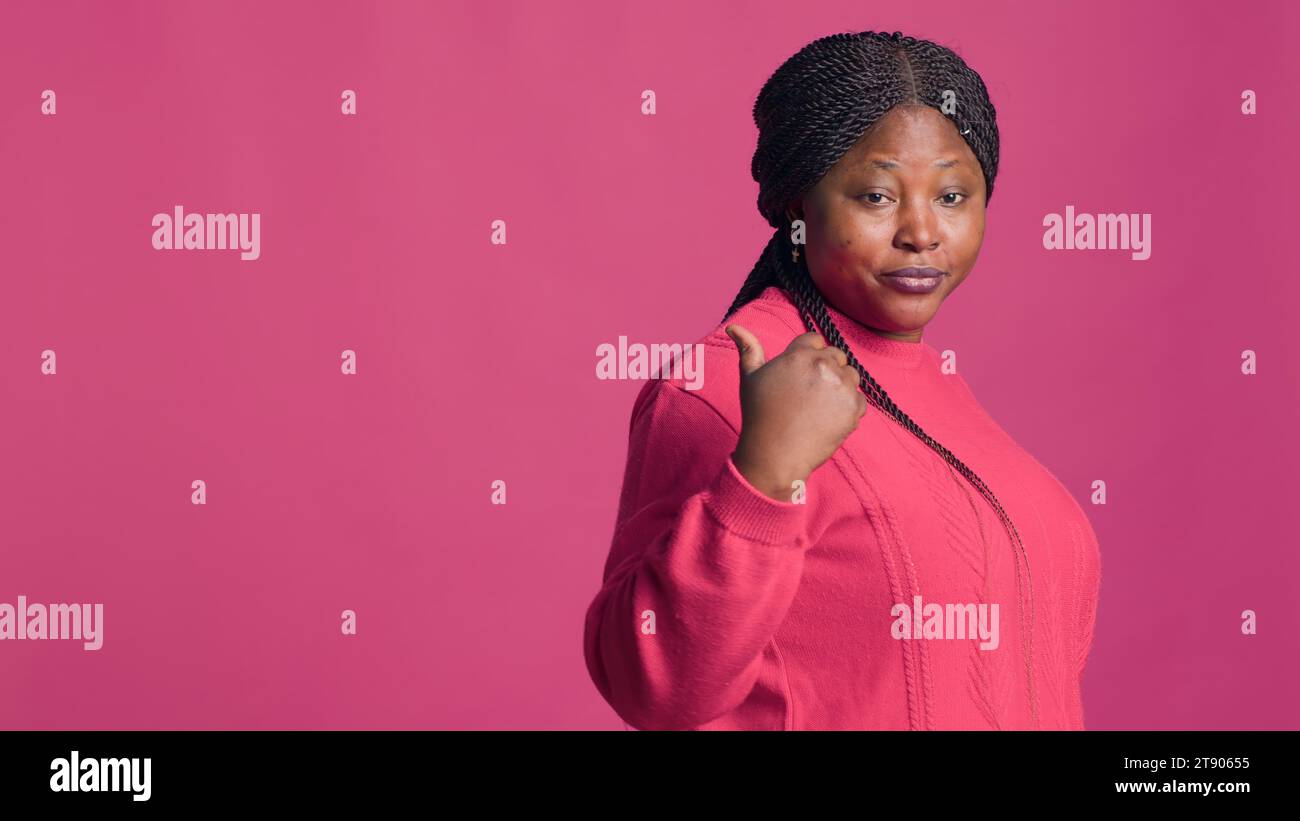 Video shot of glamorous black woman in stylish pink sweater outfit using to hand gesture to say come, lets go. African american fashionista with elegant style motioning with right-hand. Stock Photo