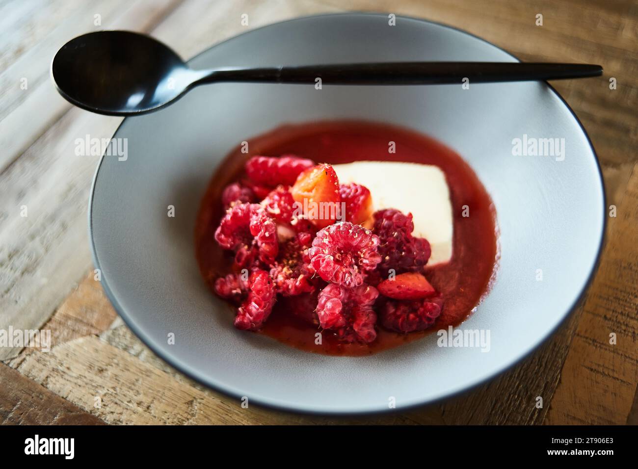Gourmet dessert of strawberries and raspberries with fresh cream in a dish with spoon on a wooden table Stock Photo