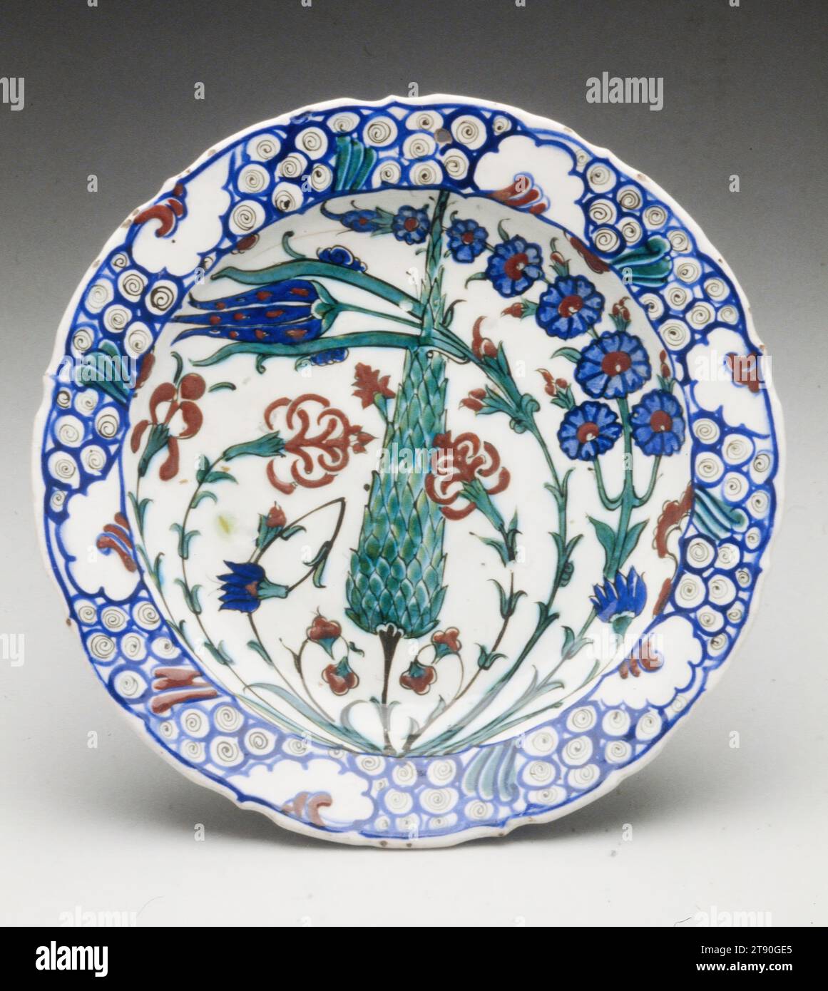 Plate, 16th century, 11 3/8 in. (28.89 cm), Iznik ware Slip-coated earthenware with blue, red and green pigments under a clear glaze,, Turkey, 16th century, This brilliant plate exemplifies the Ottomans' successful attempt at polychromy, in which a clear white body (tin-glazed earthenware) forms the ground for bright blue, green, and red underglaze motifs. The foliate rim is decorated in a stylized wave pattern ultimately based on a Chinese prototype. Because Ottoman sultans amassed large collections of Chinese ceramics, imported wares naturally influenced local production. Stock Photo