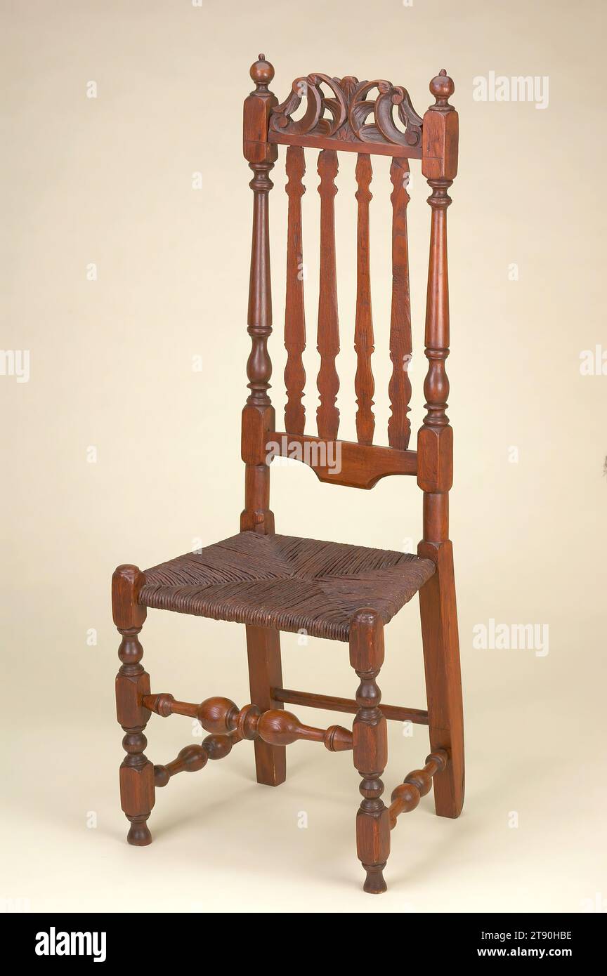 Bannister-back side chair, c. 1720, H.47-3/8 x W.17-15/16 x D.14-1/8 in., Maple and oak with rush seat, United States, 18th century, The banisters that make up the back of this chair were split in half after they had been turned on a lathe. The bannisters' flat side faces the front, where they would meet the sitter's back, and rounded side faces the rear. The manufacturing method was more labor-intensive than simple ladder-back chairs with horizontal back splats, yet less costly than their leather-upholstered or caned contemporaries. This chair descended in the family of the original owners Stock Photo