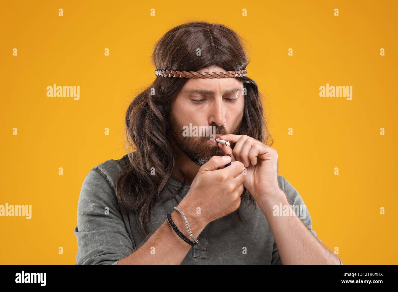 Hippie man lighting cigarette on orange background Stock Photo