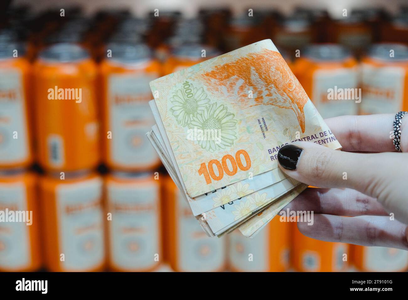 Person Holding A Stack Of Argentine Pesos. Supermarket Shelves Background. Image With Orange Tones and Image With Space For text Stock Photo