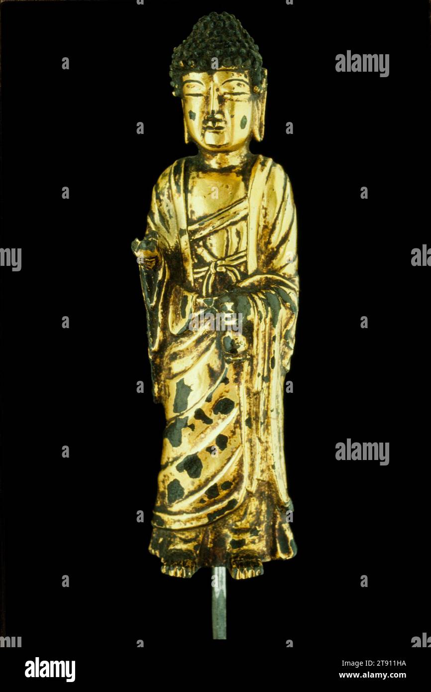 Standing Buddha, 8th century, Unknown Korean, 6 1/4 x 1 3/8 in. (15.88 x 3.49 cm), Gilt bronze, Korea, 8th century, During the Unified Silla period (668–935), Buddhism was promoted not only for the salvation of individual worshippers but also for the Korean nation as a whole. Buddhist temples proliferated and bronze images were cast in great number. Artists created small statues like this for use on family altars. While earlier images reflect sculptural styles prevalent in China, the somewhat blocky proportions, stern expression, and simplified drapery pattern of this Buddha Stock Photo
