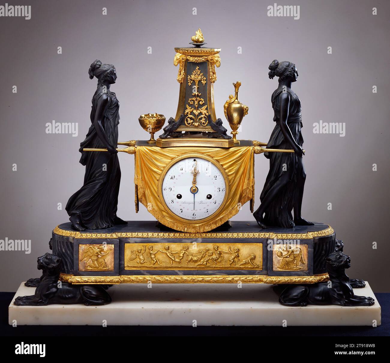 Clock with vestals, c. 1790, Pierre-Philippe Thomire; Manufacturer: Clockworks by Sauvageot, French, Paris, 20 1/2 x 25 1/2 x 7 in. (52.07 x 64.77 x 17.78 cm), Bronze, gilt bronze, enameled dial, marble, France, 18th century, French queen Marie-Antoinette, when told that her people had no bread to eat, allegedly said, 'Then let them eat cake.' The story is untrue, but she did seem out of touch with the common man. For example, she had a clock just like this in her bathroom at a time when wealthy individuals might have one clock in the whole house. Stock Photo