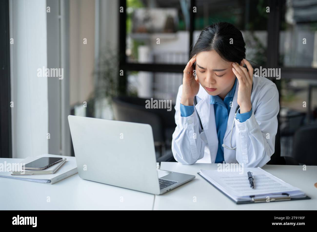 Fatig A tired and overworked Asian female doctor is suffering from headache ...