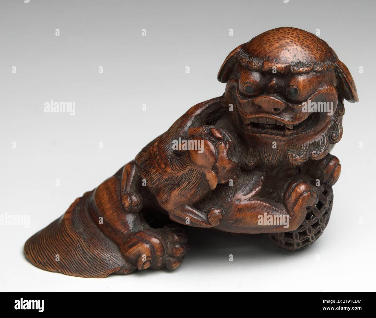 Buddhist Lion-Dog, c. 1800, 2-1/2 x 3-1/2 x 1-7/8 in. (6.4 x 8.9 x 4.8 cm), Bamboo root, China, 18th-19th century, Exquisitely carved from bamboo root, this small scholar's object represents a bushy-maned Buddhist lion-dog (shi zi) with two cubs and a pierced ball. The ball symbolizes the Buddhist jewel of truth that the lion dog protects. The theme is likely taken from fine-line paintings of Buddhist divinities, which often included fantastic beasts such as these. In style and technique, this sculpture is closest to the work of Shi Qiji also called da sheng. He was a second generation member Stock Photo