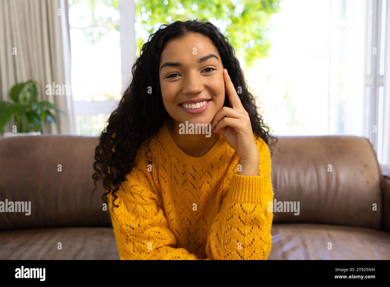 Happy biracial woman in yellow sweater making video call at home Stock Photo
