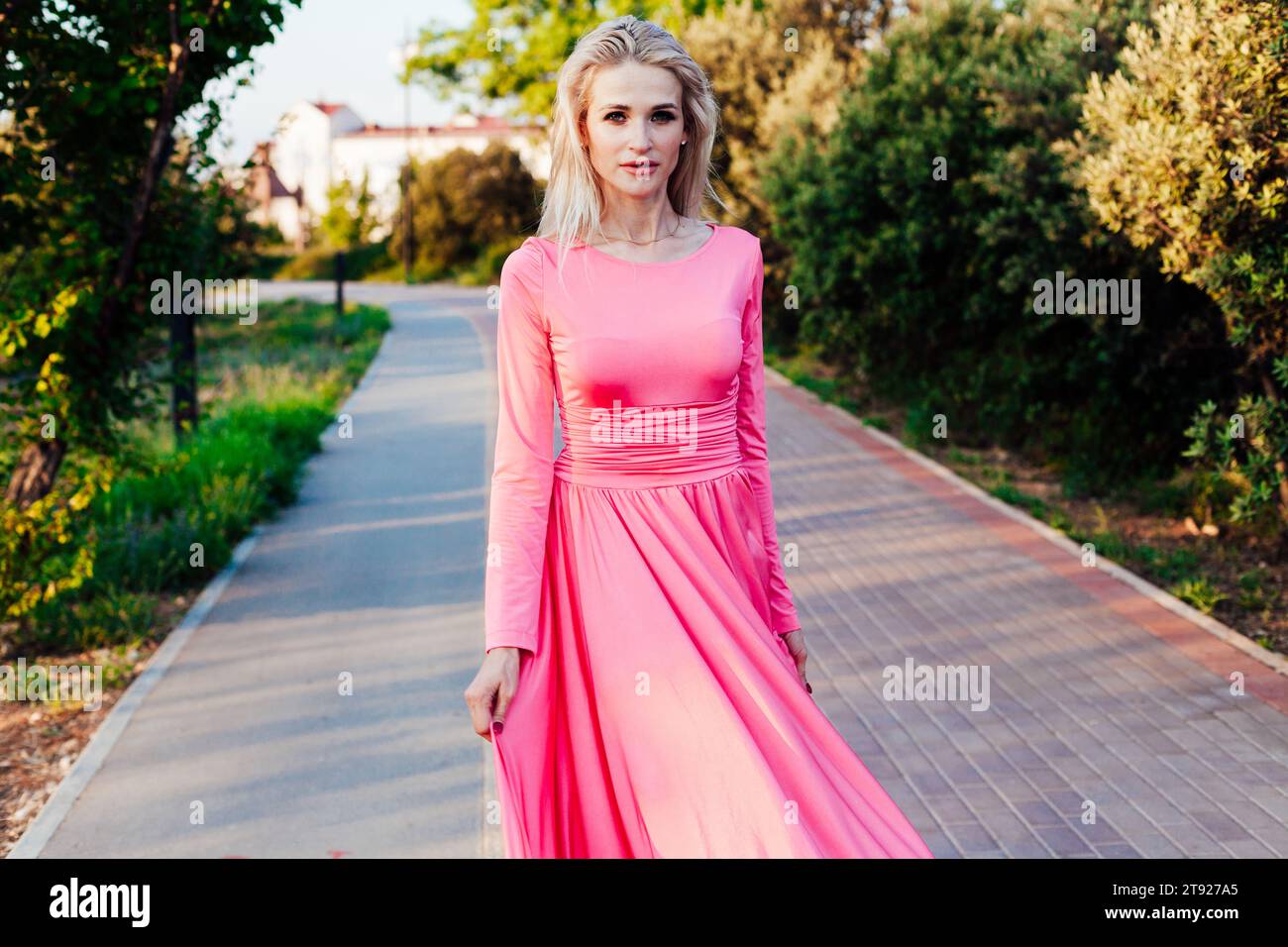 Portrait of beautiful blonde woman in pink dress in park on walk Stock Photo
