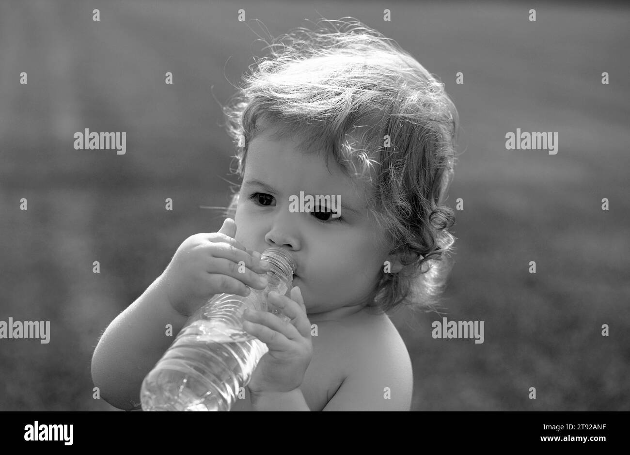 Baby drinking water. Child drinking water from bottle outdoor on grass background. Stock Photo