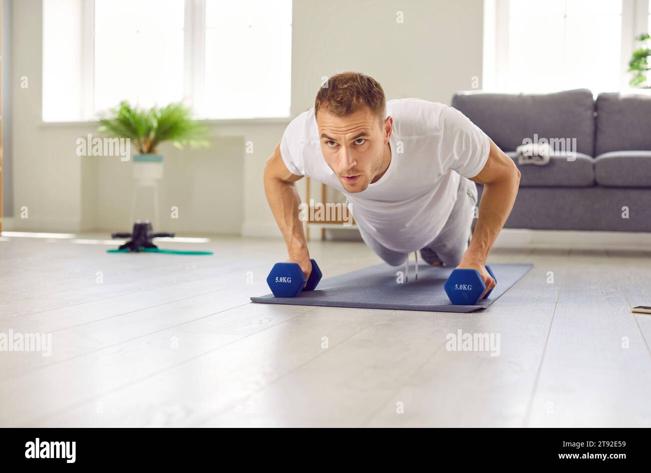 Portrait of serious sports man who does sports at home and trains muscles using dumbbells. Stock Photo