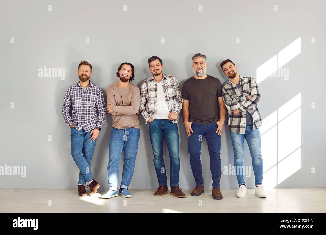 Male bearded friends looking cheerful at camera and smiling on grey ...
