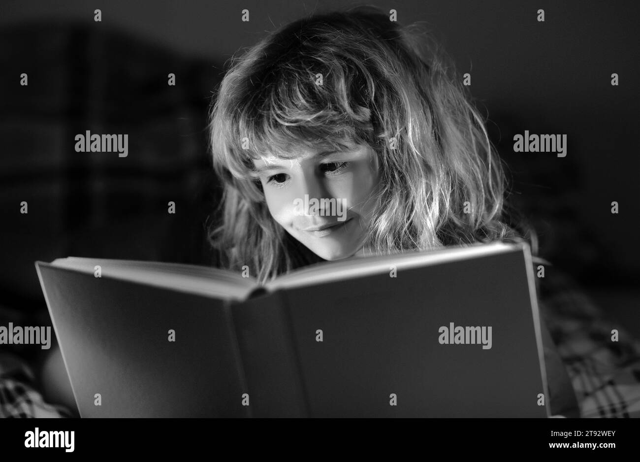 Child reading bedtime story in dark room. Cute little boy reading book