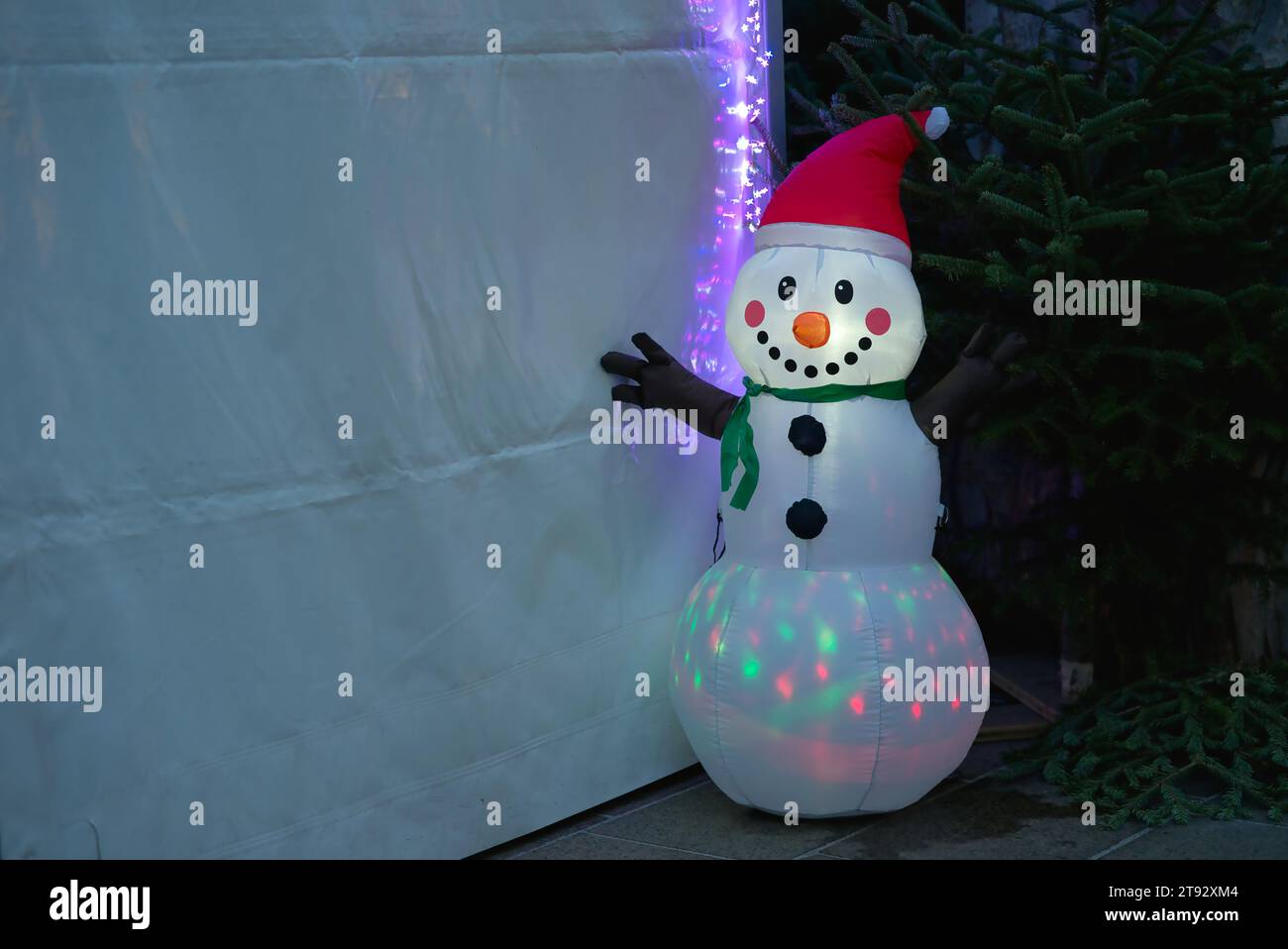 Embrace the whimsy of an inflatable snowman adorned with a red Christmas hat, internally illuminated by vibrant LED lights. With a friendly, smiling f Stock Photo