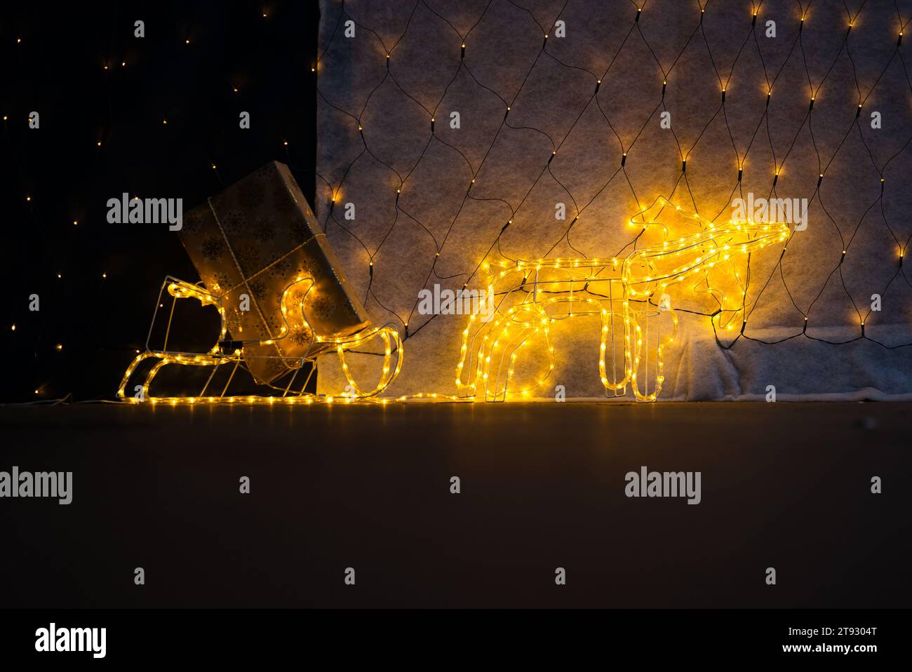 Immerse yourself in the whimsical charm of a lighted reindeer pulling a sled adorned with twinkling lights and a golden Christmas gift. The lower thir Stock Photo