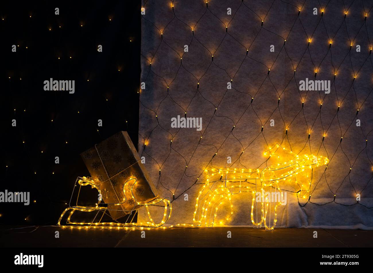 Immerse yourself in the whimsical charm of a lighted reindeer pulling a sled adorned with twinkling lights and a golden Christmas gift. The lower thir Stock Photo