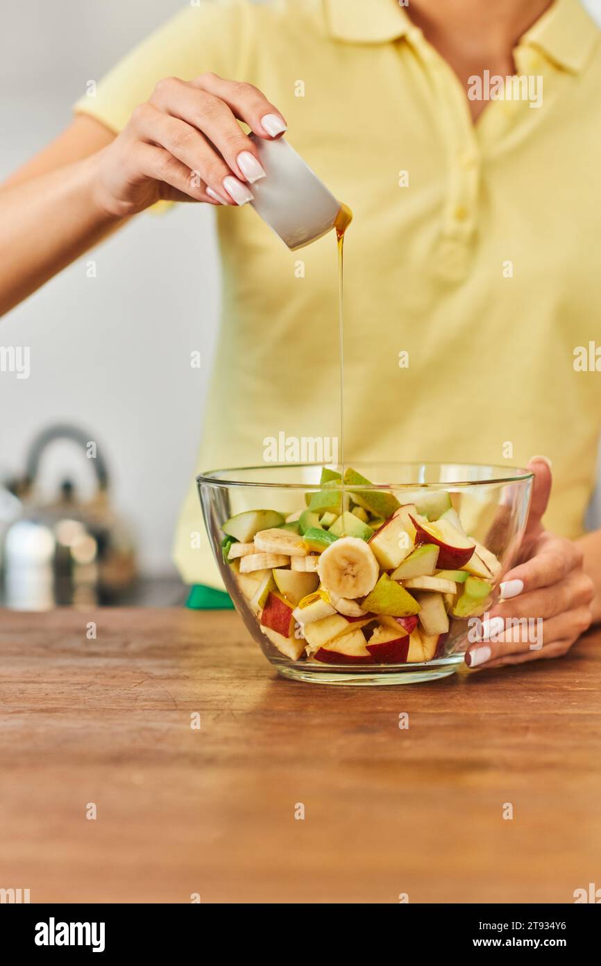 cropped view of woman pouring honey on fresh fruit salad in glass bowl