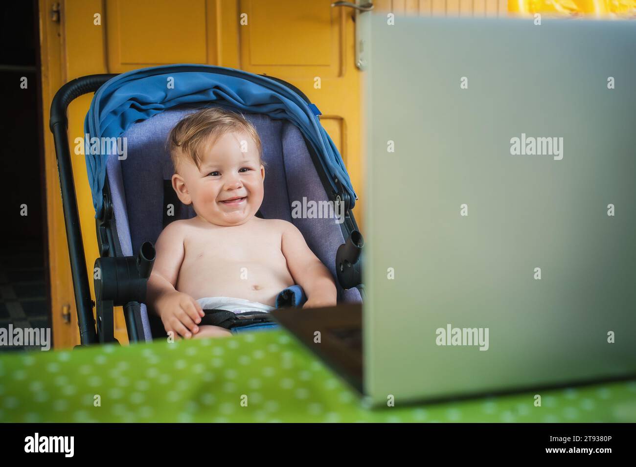Happy baby boy sitting and watching cartoons on modern wireless computer laptop. The child smiles in a cheerful mood Stock Photo